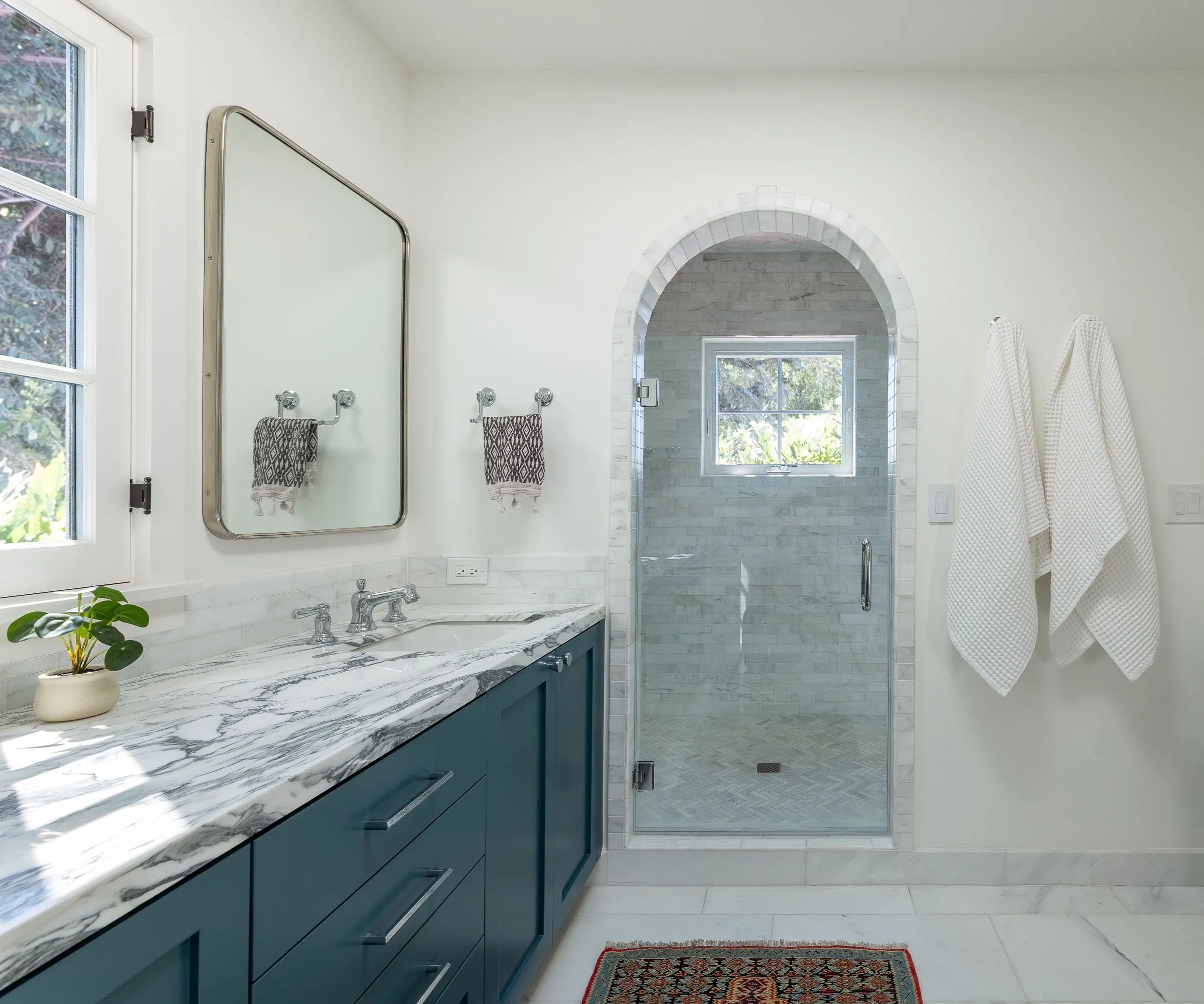 חדר רחצה גדול עם קירות לבנים כיור כחול כהה ומשטחי שיש' loading='lazy' title=