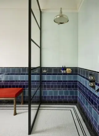 cabina de ducha con azulejos azules y blancos, puerta de vidrio, espacio de almacenaje, ducha de latón