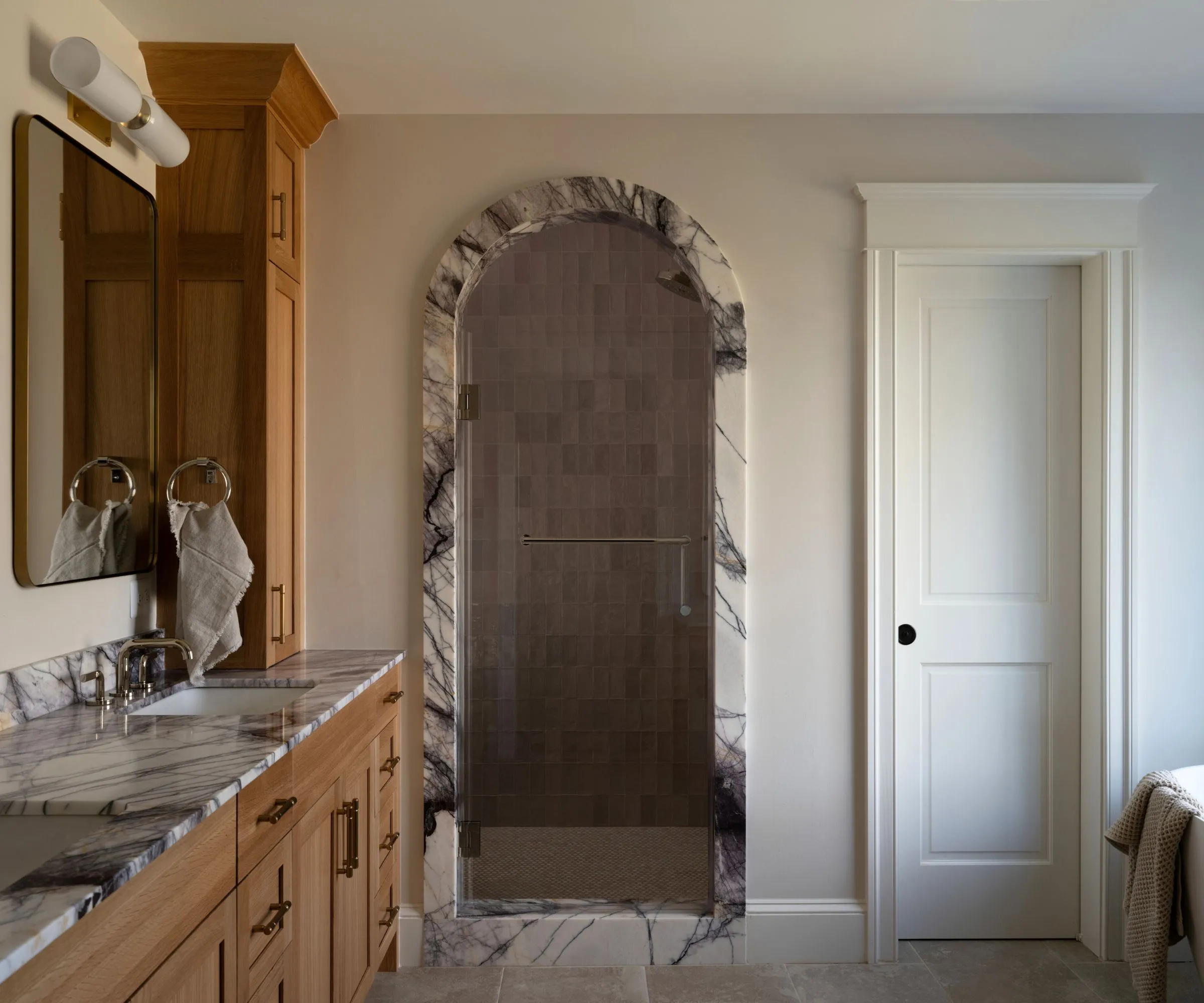 חדר אמבטיה ניטרלי חם עם יהירות עץ ושולי שיש המקיפים את קשת המקלחת' loading='lazy' title=