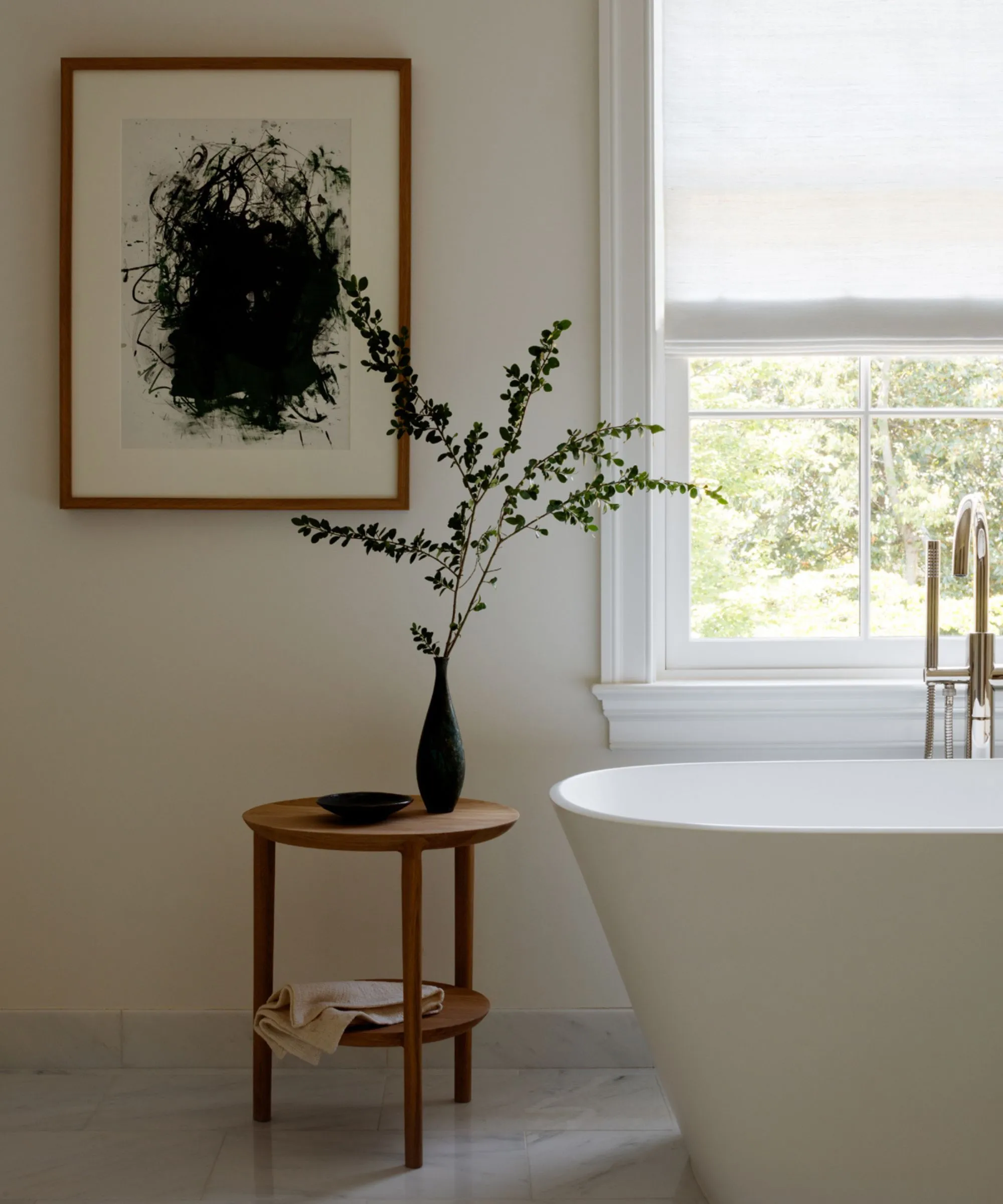 חדר אמבטיה דמוי ספא ניטרלי עם קירות לבנים חמים ריצוף אריחים באמבטיה בודדת לבנה ושולחן צד מעץ ועליו אגרטל מלא בירק' loading='lazy' title=