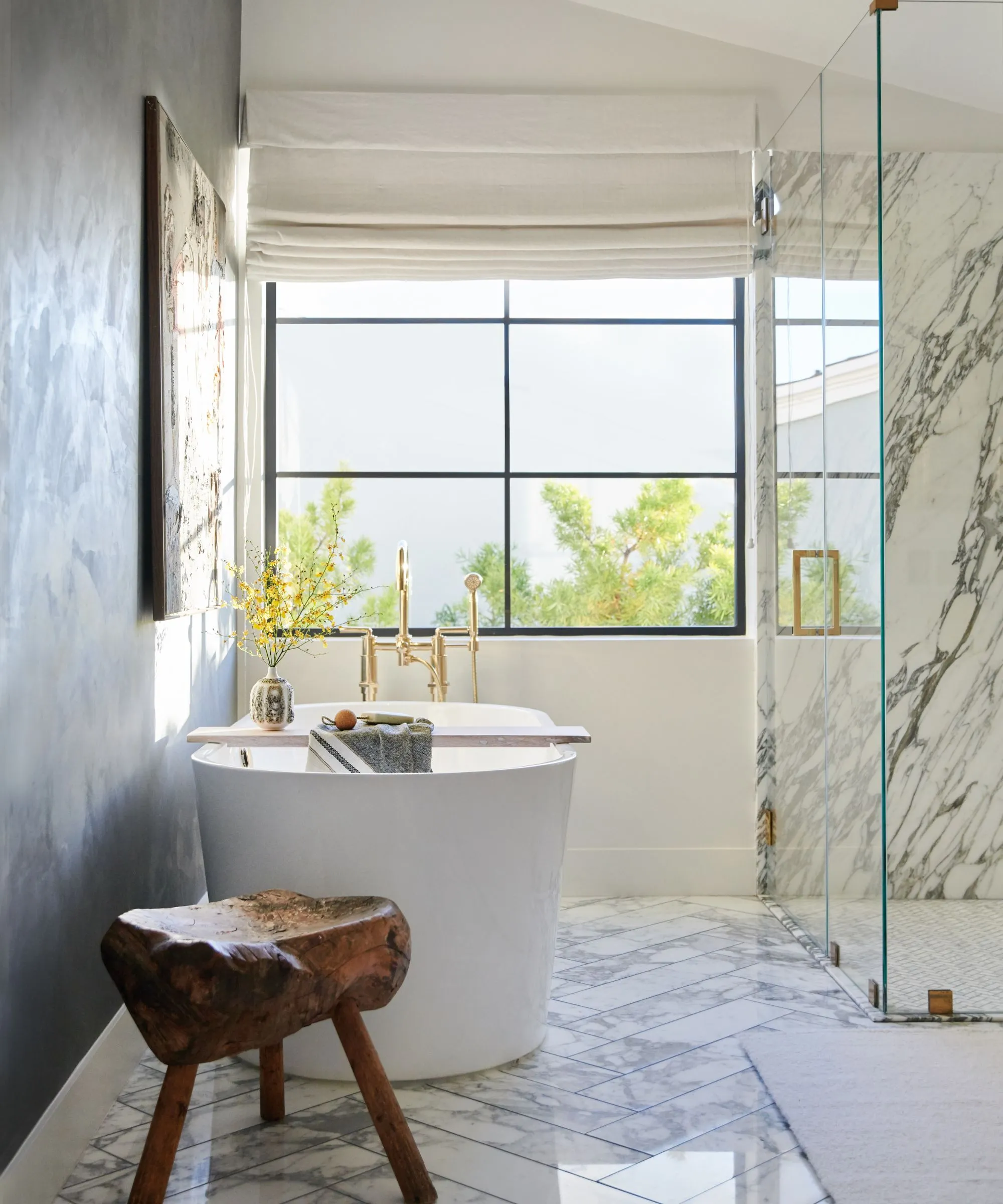 חדר אמבטיה לבן עם רצפות שיש מארז מקלחת זכוכית גדול ואמבט בודד מתחת לחלון גדול' loading='lazy' title=