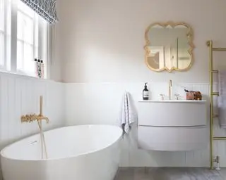 Une idée pour une petite salle de bain montrant un mur lambrissé blanc avec de la peinture rose tendre, des meubles blancs et des accessoires en or brossé