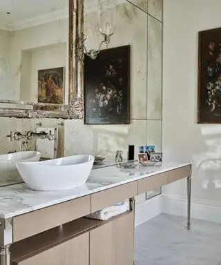 Une salle de bain avec plans de travail effet marbre et lavabo blanc devant un grand miroir