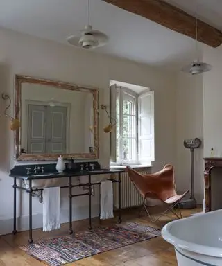 Salle de bain neutre, parquet, comptoir double vasque vintage, tapis au sol, chaise papillon en cuir