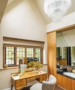 Salle de bain avec coiffeuse et chaise devant la fenêtre, lavabo en bois, lustre en verre suspendu au plafond
