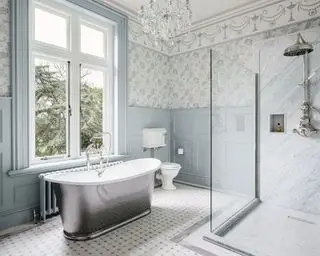 Une salle de bain avec lustre, baignoire îlot et papier peint bleu et blanc