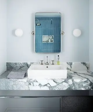 Salle de bain peinte en bleu avec carrelage bleu, comptoir en marbre avec lavabo et miroir