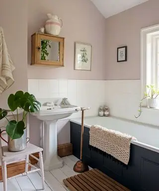 Salle de bains peinte en rose avec carrelage blanc et baignoire peinte, plantes et accessoires en bois
