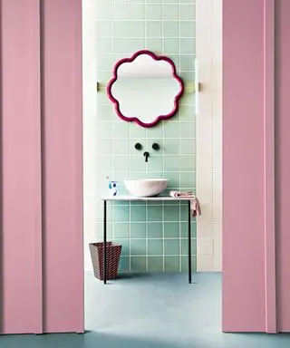 Salle de bains rose et bleue, murs peints en rose avec carrelage bleu et blanc et miroir festonné rose au-dessus du lavabo