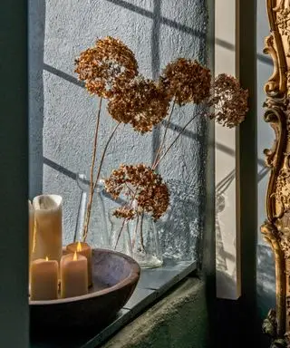 Nærbilde av bolle med stearinlys og tørkede blomster i glassvase på vinduskarmen.