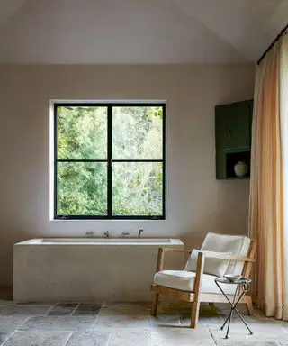 banheiro neutro com banheira de calcário, cadeira branca e piso de pedra