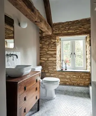 salle de bains de ferme avec mur en pierres apparentes et lavabo en bois