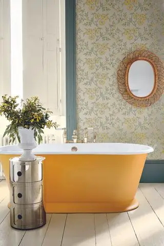 Badezimmer mit gelb gestrichener Badewanne, Tapete mit gelbem Blumenmuster, Korbspiegel, Ablage aus Metall