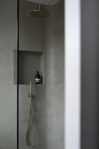 cabina de ducha con paredes de color gris medio, estante empotrado y cabezal de ducha de latón