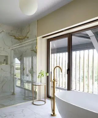 Stort badeværelse med bruseniche, marmorgulv og vægfliser, gulv til loft døre/vinduer, stor rund pendel, hvidt badekar med gulvstående vandhane