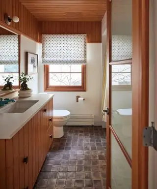 salle de bain étroite avec boiseries, plafond à feuillus, sol carrelé, store, plan de travail blanc