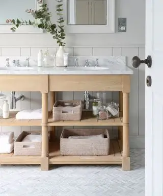 헤링본 타일 바닥, 밝은 목재 캐비닛, 싱크대, 대리석 조리대 및 보관 바구니를 갖춘 욕실