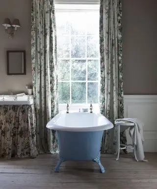 Idées de rideaux de salle de bain avec des rideaux fleuris encadrant une vue sur le jardin, avec baignoire autoportante bleue