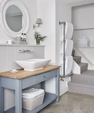 회색 테이블 위에 흰색 세면대, 타일 바닥, 흰색 수건이 달린 수건 걸이가 있는 욕실.