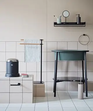 Un bagno con pareti e piastrelle rosa pallido e un lavabo verde freestanding con sopra una mensola nera
