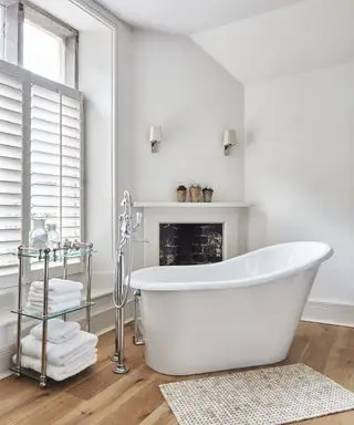 Un bagno bianco con vasca indipendente, portasciugamani e caminetto ornamentale