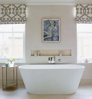 Un bagno color crema con vasca autoportante e mensola in una nicchia