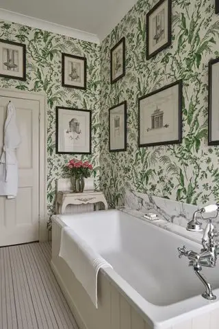 Un exemple d'idées de salle de bain verte montrant une salle de bain traditionnelle avec du papier peint vert botanique et des œuvres d'art sur les murs.