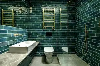 Une salle de bains verte avec des carreaux muraux verts, des luminaires et des accessoires en laiton et une porte de douche en verre