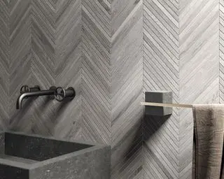 Carrelage de salle de bain en diagonale grise de Lapicida derrière un lavabo en pierre grise.