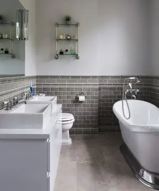 salle de bain de style traditionnel avec baignoire sabot, deux vasques et carrelage gris foncé. Murs peints en gris et sol gris foncé.