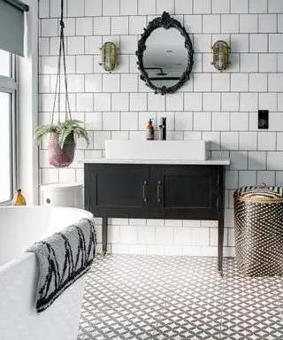 Salle de bain avec mur et baignoire en carrelage blanc, sol en carrelage géométrique gris et blanc, lavabo noir et blanc et touches décoratives colorées.