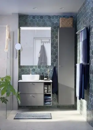 Une salle de bains bleue avec du carrelage bleu dans une pièce humide neutre avec un meuble vasque suspendu et un porte-serviettes