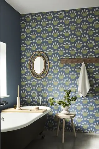 Une salle de bains bleue avec du papier peint vert et bleu avec un miroir en rotin et une tringle à chevilles