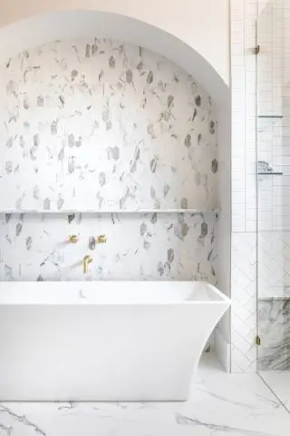 Un exemple d'idées de salle de bain spa montrant une salle de bain blanche avec des carreaux de différentes formes en marbre et métro avec une baignoire blanche