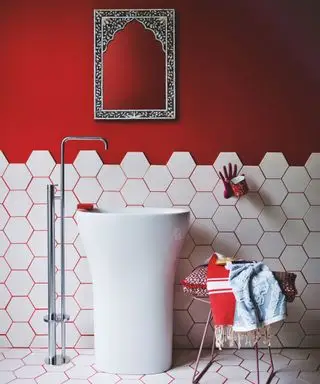Cuarto de baño pintado de rojo con azulejos blancos y lechada roja, lavabo alto con grifo de suelo