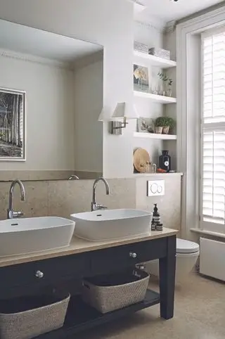 Badezimmer mit Waschtisch mit Doppelwaschbecken, Toilette und Regalen darüber, neutralen Boden- und Wandfliesen und weißen Wänden darüber