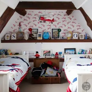 Ideen für ein gemeinsames Schlafzimmer im Dachgeschoss mit einer roten Flugzeugtapete, Decken und Spielzeug, die von der Decke hängen, eingebauten Holzregalen und einer Truhe.