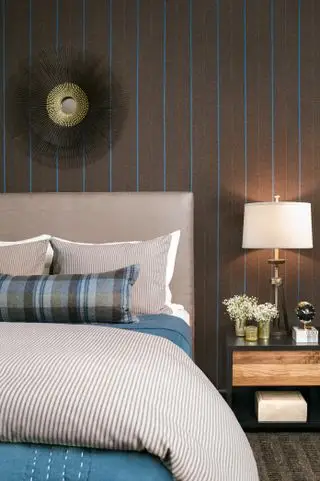 Sypialnia z łóżkiem z tapicerowanym zagłówkiem, lustrem na ścianie z brązowo-niebieskim paskiem i szafką nocną