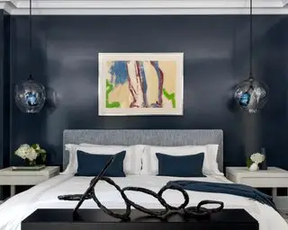 Et hovedsoverom som viser ideer til et soverom med marineblå glansmalte vegger og statement-kunstverk, inkludert en skulptur i enden av sengen