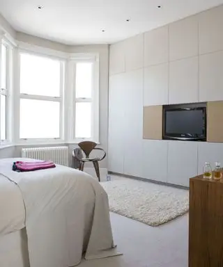 Une idée de télévision dans une chambre avec un lit et une décoration murale blancs, avec une télévision installée dans le cadre d'une armoire blanche