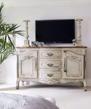 Une idée de téléviseur de chambre à coucher avec une télévision murale au-dessus d'un buffet antique en détresse de couleur crème