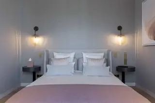 곡선형 헤드보드와 벽 조명이 있는 핑크와 그레이 색상의 Ina Rinderknecht 침실