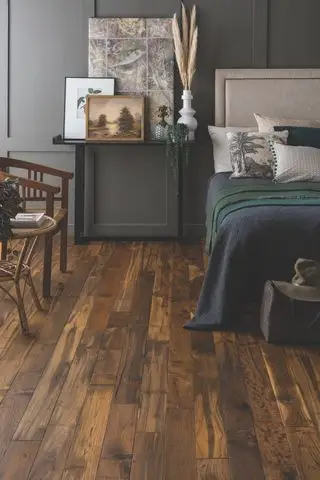 Chambre avec lit et table de nuit, chaise et table d'appoint, murs lambrissés gris et parquet en bois foncé