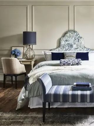 blått og hvitt soverom med taupe vegger, blått og hvitt sengetøy, fotskammel, tregulv, blå lampe, lenestol, sidebord
