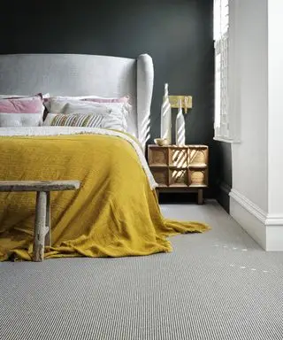 Et svart soverom med en blekgrå seng og sennepsgul sleng