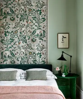 Un letto con un plaid rosa davanti a un muro floreale verde e rosa