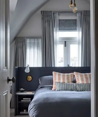 Et soverom med en blå seng og vinduer med ekstra rene gardiner og en mønstret persienn