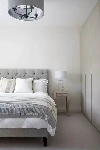 chambre grise et blanche avec lit à boutons gris, table d'appoint antique, lampe blanche, armoires encastrées, suspension grise