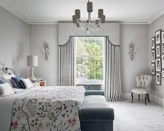 Spálňa s manželskou posteľou, krbom, pásovým oknom, garnižou a závesmi a prikrývkou s kvetinovým vzorom.