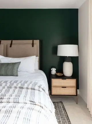 schema di camera da letto neutra con parete dipinta di verde foresta dietro il letto, comodino in legno nero e vimini, lampadario bianco, testiera imbottita color farina d'avena, biancheria da letto bianca, coperta a righe bianche e grigie, cuscino grigio